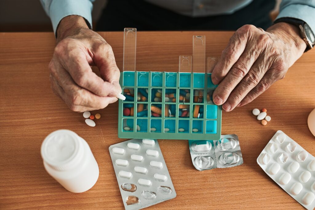 Senior adult using a pill organizer with caregiver assistance, managing multiple medications safely at home.